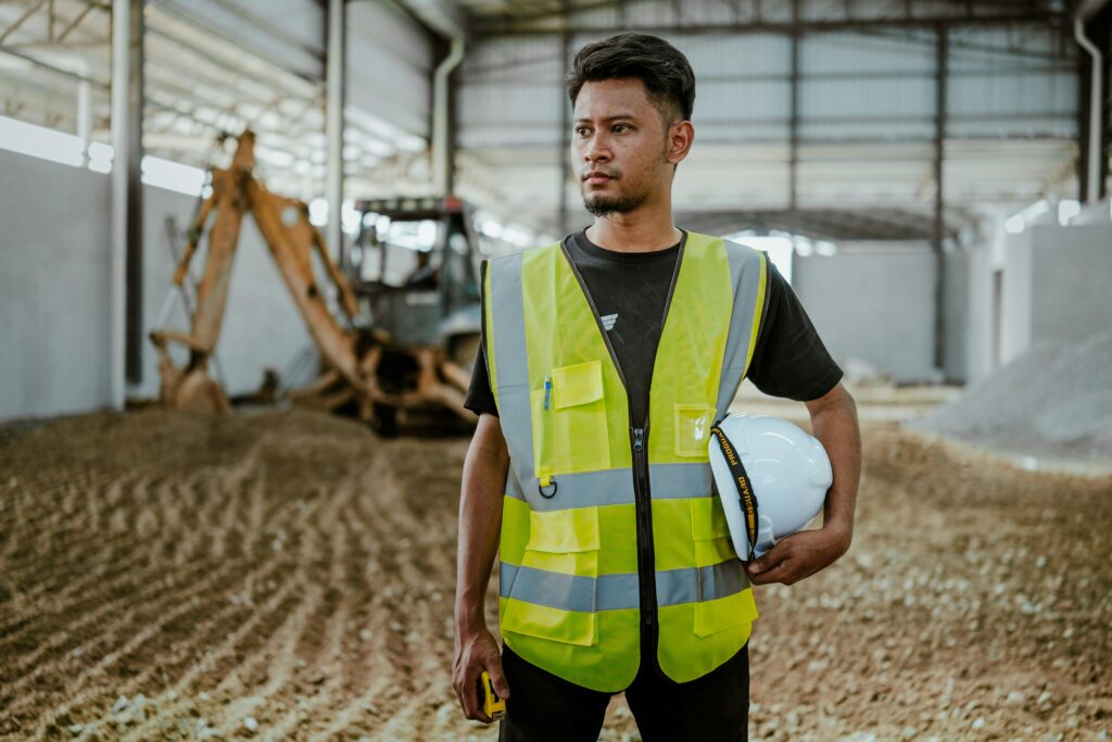 Portrait of a construction worker in safety gear holding a helmet inside an industrial setting.